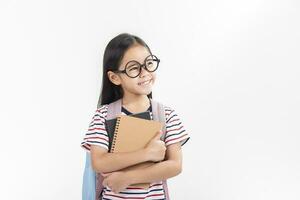 Chica de escuela abrazando libro vistiendo mochila sonriente aislado en blanco antecedentes foto