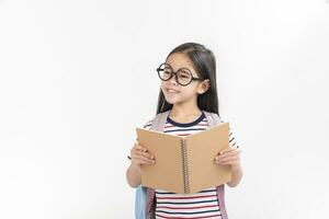 Chica de escuela abrazando libro vistiendo mochila sonriente aislado en blanco antecedentes foto