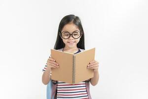 Chica de escuela abrazando libro vistiendo mochila sonriente aislado en blanco antecedentes foto