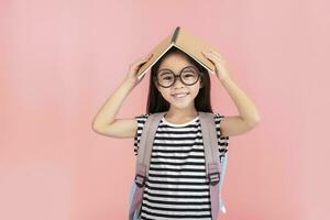 schoolgirl hugging book wearing backpack smiling isolated on pink background photo