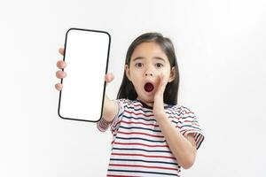 asiático pequeño niña participación teléfono inteligente Bosquejo de blanco pantalla y sonriente en blanco antecedentes. foto