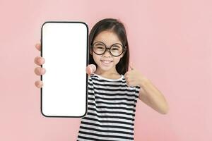 asiático pequeño niña participación teléfono inteligente Bosquejo de blanco pantalla y sonriente en blanco antecedentes. foto