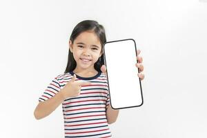 asiático pequeño niña participación teléfono inteligente Bosquejo de blanco pantalla y sonriente en blanco antecedentes. foto