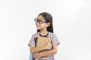 Chica de escuela abrazando libro vistiendo mochila sonriente aislado en blanco antecedentes foto