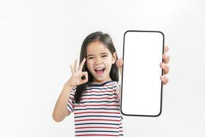 asiático pequeño niña participación teléfono inteligente Bosquejo de blanco pantalla y sonriente en blanco antecedentes. foto