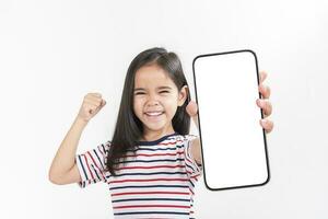 asiático pequeño niña participación teléfono inteligente Bosquejo de blanco pantalla y sonriente en blanco antecedentes. foto