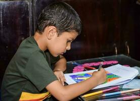 Smart Indian little boy drawing with colourful pencils kit of various colours during the summer vacations, Cute Indian Kid Sketching colourful drawing on wooden table photo