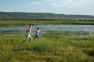 Two brothers in jeans and t-shirts run along the pond competing in speed. Summer sunny day near the pond. Summer holidays in the countryside photo
