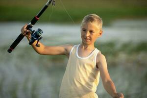 Little boy is fishing at sunset on the lake photo