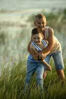 Two brothers in jeans and t-shirts have fun and laugh near the pond. Summer sunny day near the pond. Summer holidays in the countryside. Happy childhood photo