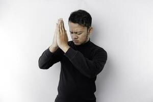 Religious Asian man wearing a black shirt praying to God, isolated by a white background photo