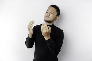 Religious Asian man wearing a black shirt praying to God, isolated by a white background photo