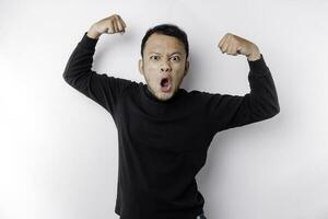 Excited Asian man wearing a black shirt showing strong gesture by lifting his arms and muscles smiling proudly photo