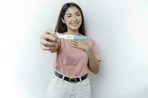 Happy mindful thankful young woman wearing pink t-shirt showing her pregnancy test, hand on chest smiling isolated on white background photo
