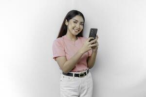 A portrait of a happy Asian woman is wearing pink t-shirt and holding her phone, isolated by white background photo