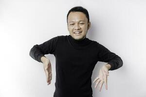 Excited Asian man wearing black shirt pointing at the copy space below him, isolated by white background photo