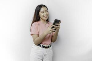 A portrait of a happy Asian woman is wearing pink t-shirt and holding her phone, isolated by white background photo