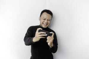 Young Asian man in casual wear is playing games with mobile phone with a white background isolated. photo