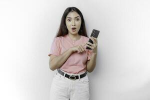 Shocked Asian woman dressed in pink and holding her phone, isolated by white background photo
