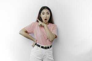 Shocked Asian woman wearing pink t-shirt, pointing at the copy space on beside her, isolated by white background photo