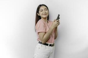 A portrait of a happy Asian woman is wearing pink t-shirt and holding her phone, isolated by white background photo