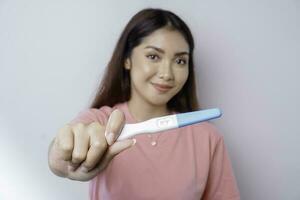 Happy young woman wearing pink t-shirt showing her pregnancy test, isolated on white background, pregnancy concept photo