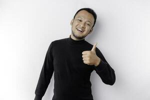 Excited Asian man wearing black shirt gives thumbs up hand gesture of approval, isolated by white background photo