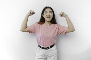 emocionado asiático mujer vistiendo un rosado camiseta demostración fuerte gesto por levantamiento su brazos y músculos sonriente con orgullo foto