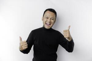 Excited Asian man wearing black shirt gives thumbs up hand gesture of approval, isolated by white background photo