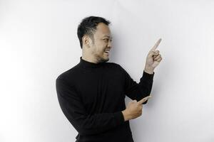 Excited Asian man wearing black shirt pointing at the copy space beside him, isolated by white background photo