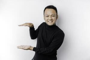 Smiling young Asian man is standing over isolated background holding copy space imaginary on the palm to insert an ad photo