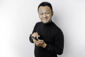 Excited Asian man wearing black shirt smiling while holding his phone, isolated by white background photo