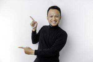 Excited Asian man wearing black shirt pointing at the copy space beside him, isolated by white background photo