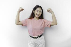 emocionado asiático mujer vistiendo un rosado camiseta demostración fuerte gesto por levantamiento su brazos y músculos sonriente con orgullo foto