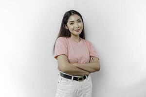 Portrait of a confident smiling Asian woman is wearing pink t-shirt, standing with arms folded and looking at the camera isolated over white background photo