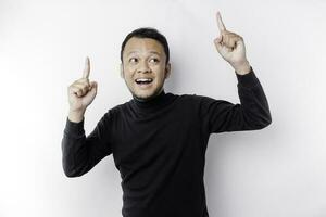 Excited Asian man wearing black shirt pointing at the copy space on top of him, isolated by white background photo