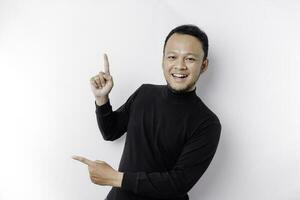 Excited Asian man wearing black shirt pointing at the copy space beside him, isolated by white background photo