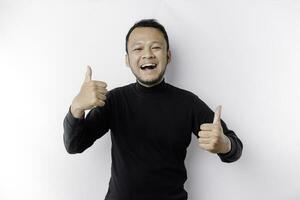 Excited Asian man wearing black shirt gives thumbs up hand gesture of approval, isolated by white background photo