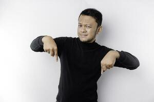 Excited Asian man wearing black shirt pointing at the copy space below him, isolated by white background photo