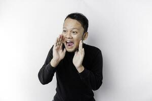 Young handsome man wearing a black shirt shouting and screaming loud with a hand on his mouth. communication concept. photo