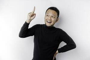 Excited Asian man wearing black shirt pointing at the copy space on top of him, isolated by white background photo