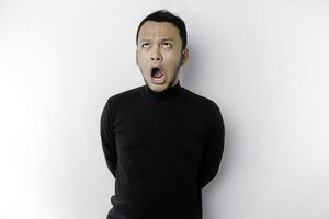 Shocked Asian man with his mouth wide open wearing black shirt, isolated by a white background photo
