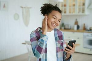 joven moderna de raza mixta escuchando música, sosteniendo un teléfono inteligente, usando aplicaciones musicales en casa foto