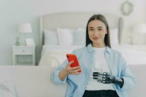 Happy girl is holding glass of water with cyber hand prosthesis. Futuristic medical technology. photo