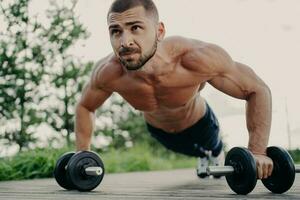 Muscular man does push-ups, focuses outdoors, trains abs with barbells. Sporty lifestyle. photo