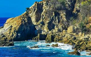 Surfer waves turquoise blue water rocks cliffs boulders Puerto Escondido. photo