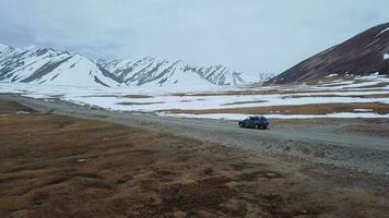 de weg tussen besneeuwd bergen en een voorbijgaan auto, antenne visie video