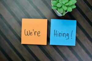 Concept of We're Hiring write on sticky notes isolated on Wooden Table. photo