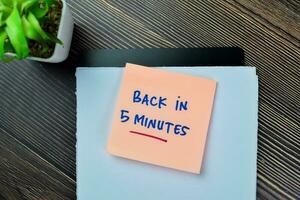 Concept of Back in 5 Minutes write on sticky notes isolated on Wooden Table. photo