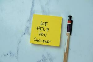 Concept of We Help You Succeed write on sticky notes isolated on Wooden Table. photo